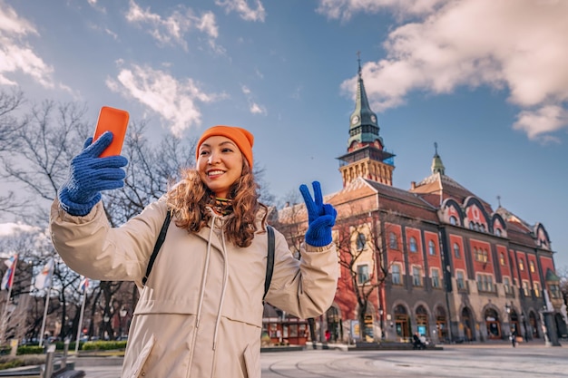 Tourist girl taking selfie photo against Subotica town hall while travelling in Serbia