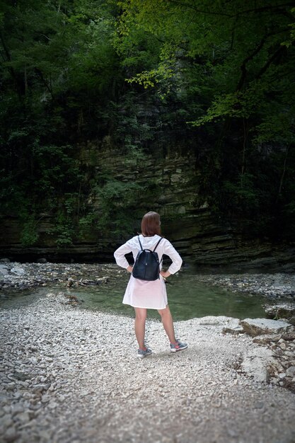 Tourist girl in white tunic inspects the sight stands with her hands on her sides view from behind