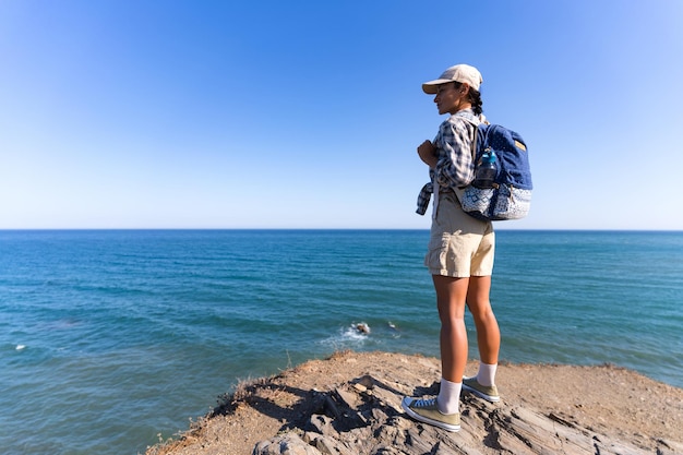 tourist girl with a backpack on her back in the summer stands on top of a mountain