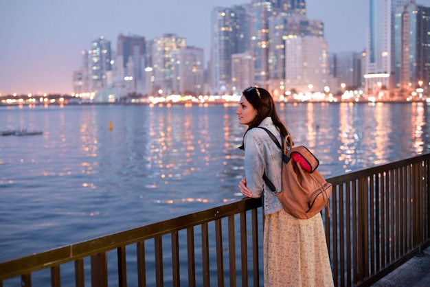 A tourist girl with a backpack on her shoulders enjoys a view of the modern