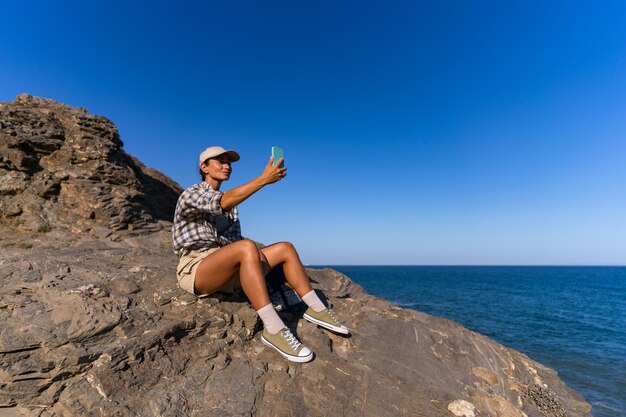 Photo tourist girl with a backpack in the summer on top of a mountain takes a selfie against the backdrop