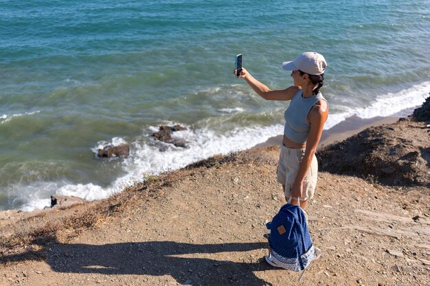 tourist girl with a backpack in the summer on top of a mountain takes a selfie against the backdrop