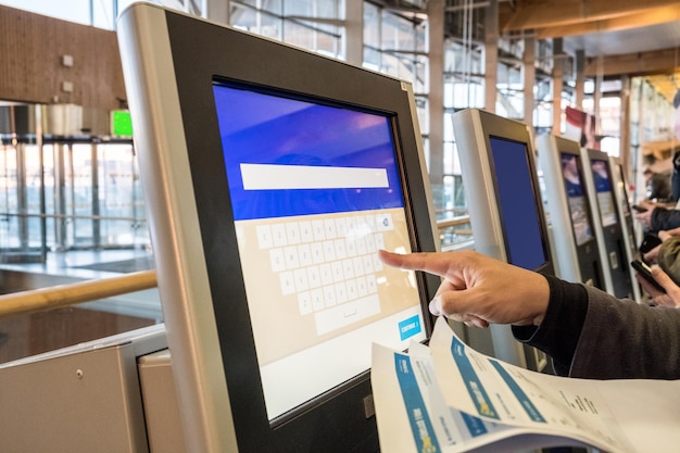 tourist hand touching display at selfservice transfer machine buying airplane or train tickets at automatic device at airport