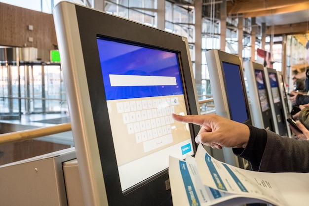 Tourist hand touching display at selfservice transfer machine buying airplane or train tickets at automatic device at airport