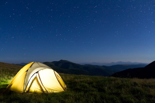 Tourist hikers tent in mountains at night with stars in the sky