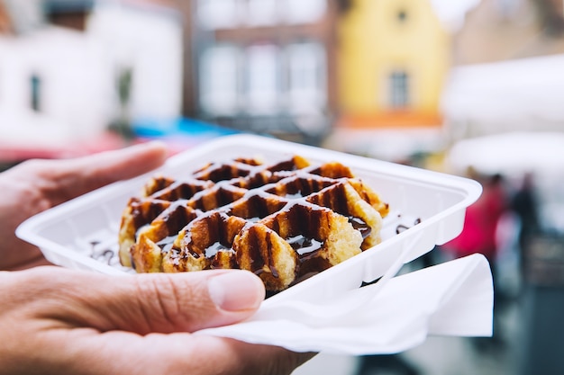 Tourist holds in hand popular street food  Belgium tasty waffle with chocolate sauce