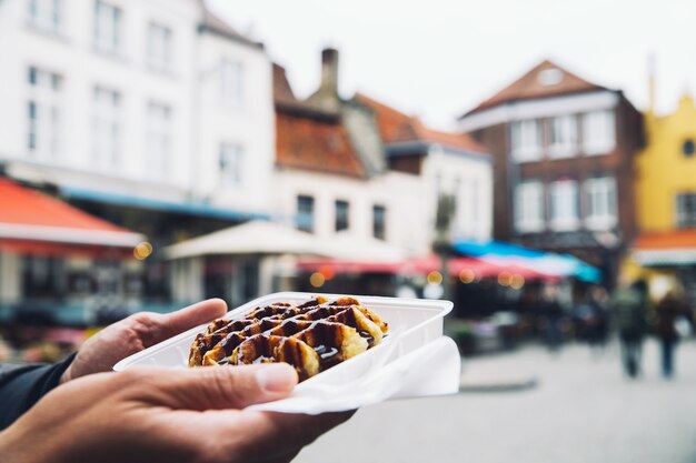 Photo tourist holds in hand popular street food  belgium tasty waffle with chocolate sauce