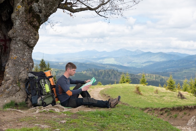 Tourist is studying a map of the area sitting under a tree by the road