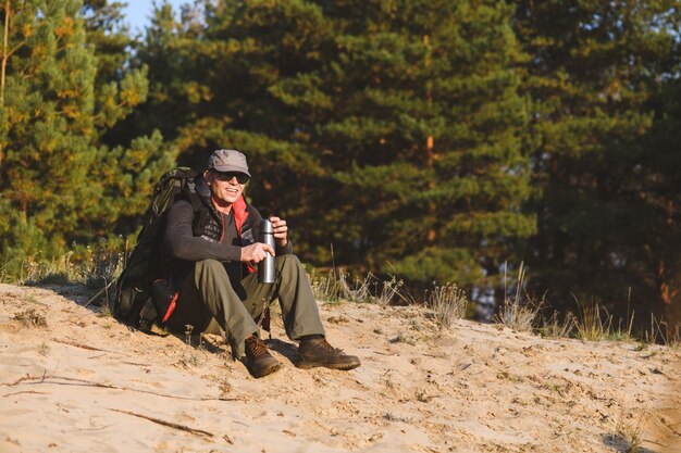 L'uomo turistico ha una pausa con il thermos nella foresta