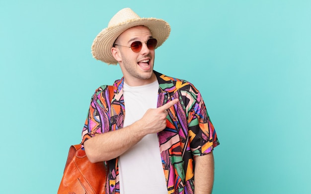 Tourist man looking excited and surprised pointing to the side and upwards to copy space