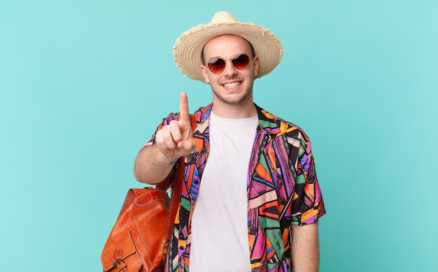 Tourist man smiling proudly and confidently making number one pose triumphantly, feeling like a leader