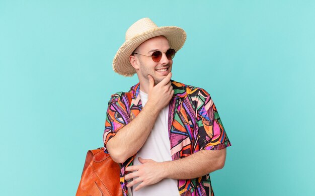 Tourist man smiling with a happy, confident expression with hand on chin, wondering and looking to the side