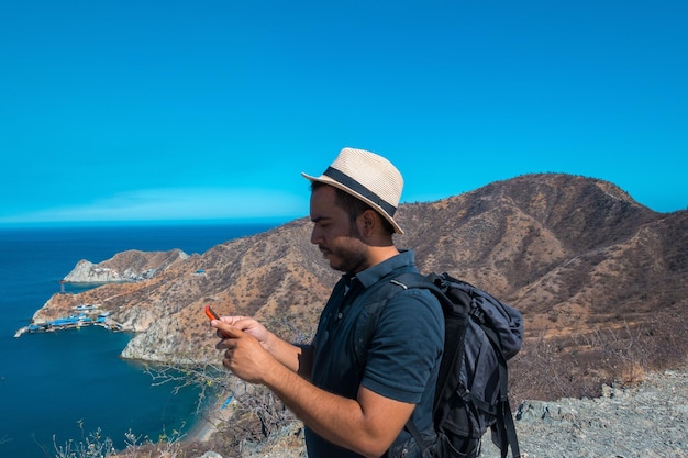 海を背景に美しい風景の上でスマートフォンを使用して観光客の男性。旅行、観光、夏休み、休暇、アクティブなライフスタイルのコンセプト