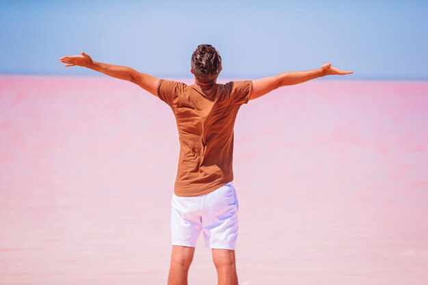 Tourist man walk on a pink salt lake on a sunny summer day.