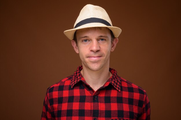 tourist man wearing red checkered shirt and hat against brown wall