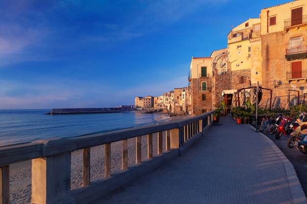 日没時の沿岸都市チェファルの旧市街、シチリア島、イタリアの観光遊歩道と空のビーチ