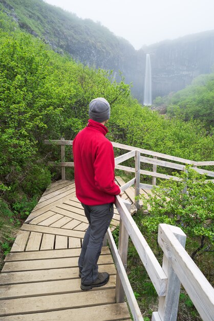 Tourist in a red jacket looking at a waterfall in Iceland