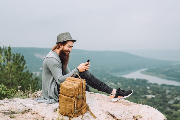 관광은 그의 손에있는 전화로 높은 바위에 앉아있다.