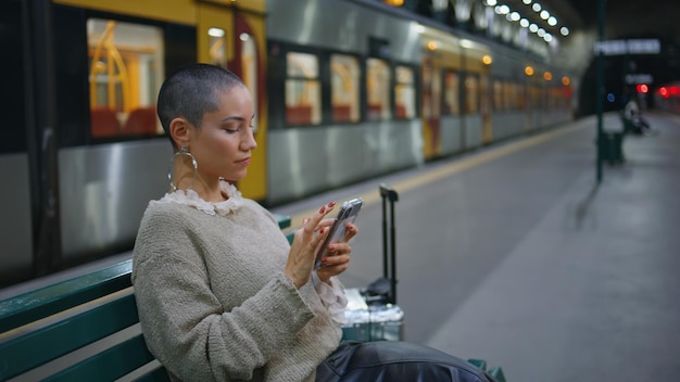 観光客が駅のベンチに座って,携帯電話のクローズアップで出発スケジュールを見ています.