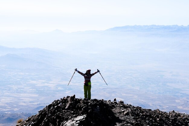 手を上げて火山の山の頂上に立っている観光客