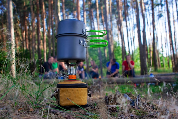 Туристическая газовая плита для кемпинга и отдыха на фоне леса и отдыхающих туристов
