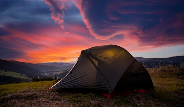 Tourist tent in the mountains under dramatic evening sky Colorfull sunset in mountains Camping travell concept Traveler people enjoying the advanture alternative vacation