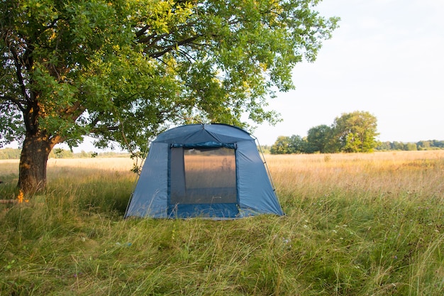 A tourist tent in nature under a tree. Summer vacation hiking