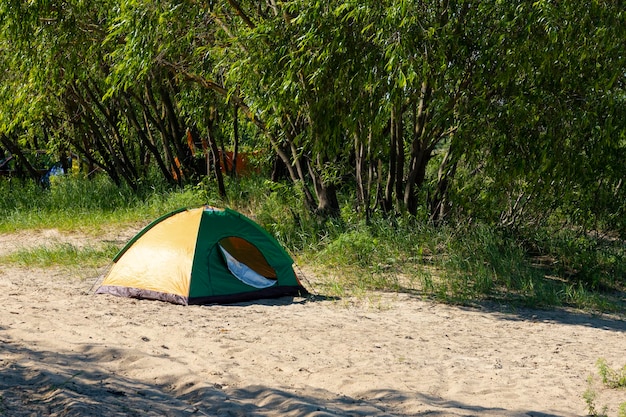 Tourist tent on the sandy bank of the river against the backdrop of green vegetation