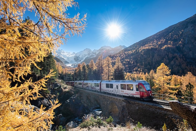 Tourist train on the swiss alps passes through mountains with glaciers and forests in autumn