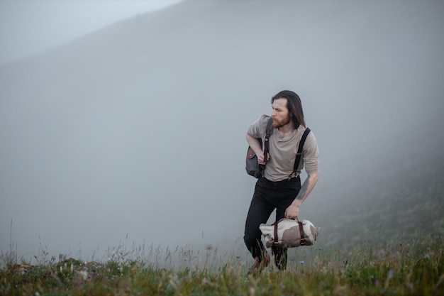 Tourist traveler hipster dressed in vintage style with backpack and plaid against backdrop of mountains in fog