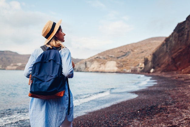 Tourist walking on Red beach by Aegean sea in Akrotiri, Santorini island, Greece. Woman with backpack traveling