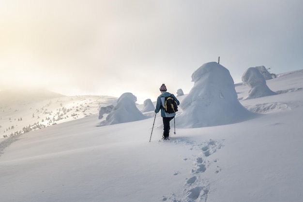 The tourist walks on deep solid snow in winter mountains