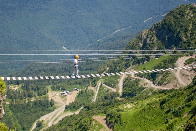 A tourist walks on a transparent rope bridge over a precipice in the Caucasus mountains, extreme entertainment.