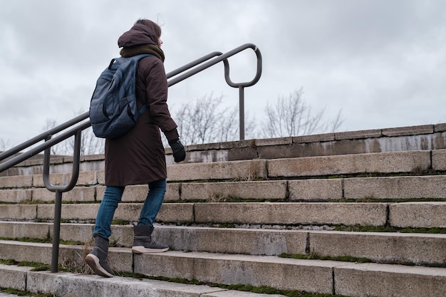 A tourist in warm clothes and a city backpack climbs the old\
stone steps of the stairs