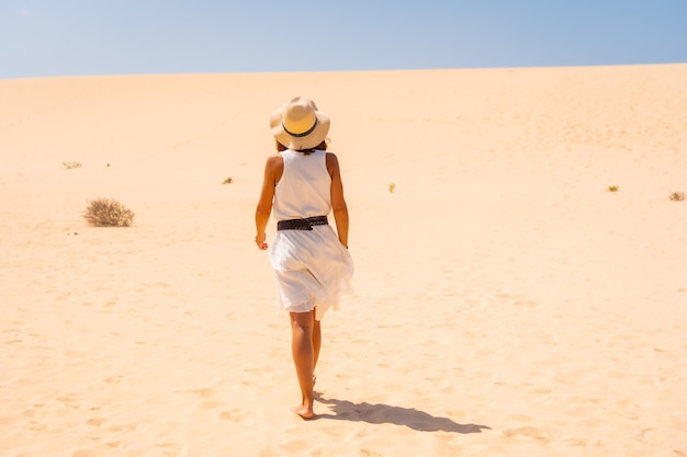흰 드레스와 모자를 쓴 관광객이 카나리아 제도 푸에르테벤투라에 있는 코랄레호 자연 공원의 모래 언덕을 걷고 있습니다. 스페인