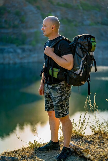 Tourist with a backpack on his shoulders stands on a rock Summer nature background A traveler looks at the landscape in front of him