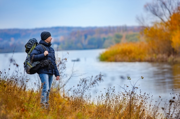 A tourist with a backpack looks at the other bank of the river in the autumn.