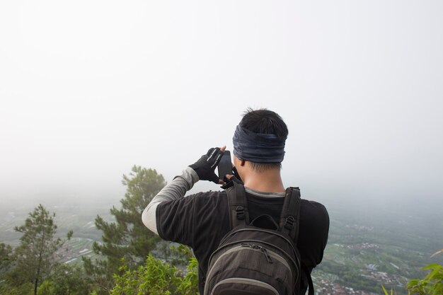 バックパックを持った観光客が山でスマートフォンで写真を撮る