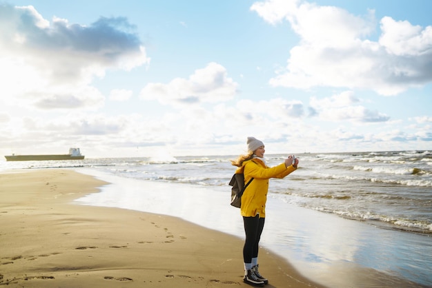 Tourist with phone Selfie time Tourist in yellow jacket posing by sea at sunset Travelling