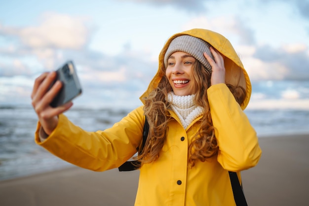 Турист с телефоном время селфи Турист в желтой куртке позирует у моря на закате Путешествие
