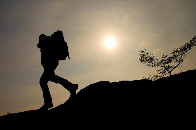 Photo tourist with sporty backpack and poles in hands stand on cliff and watching into deep misty valley