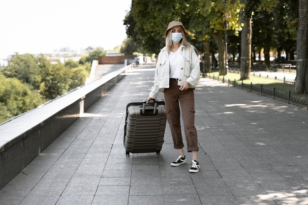 유럽 도시의 관광 여성, 유럽의 관광. 얼굴에 의료 보호 마스크를 쓴 어린 소녀가 큰 가방을 당깁니다.