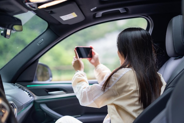 観光客の女性が道路旅行に行き車の中に座って携帯電話で写真を撮ります