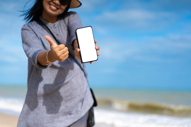 Туристическая женщина показывает пустой экран смартфона на пляже