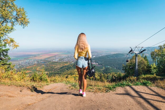観光客の女性は山の斜面に立って、リゾートタウンアルタイ地方ロシアを見下ろします