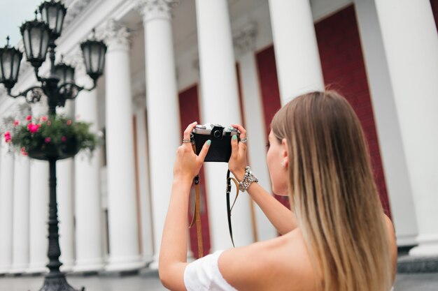 Tourist woman takes picture of a building with columns on a retro camera outdoors