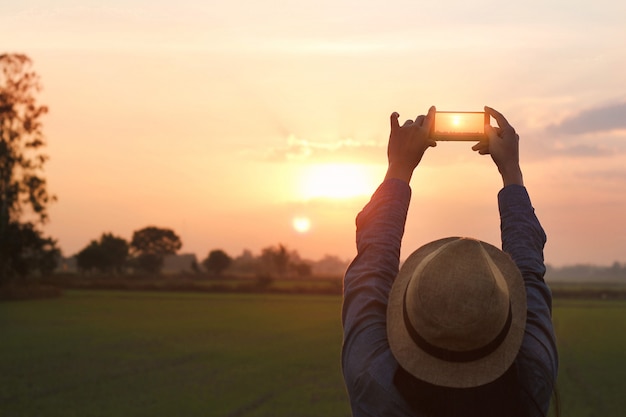 日没の自然の背景にスマートフォンで写真を撮って観光女性