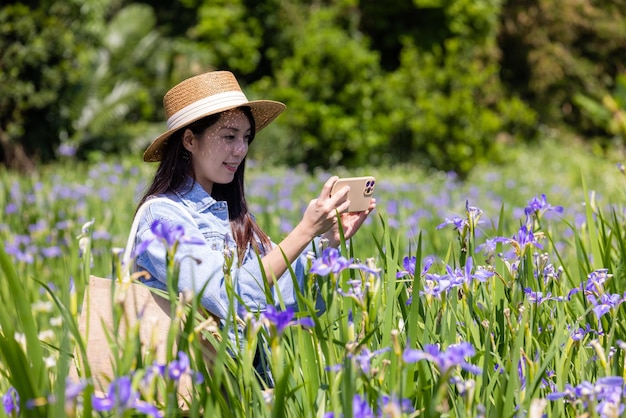 観光客の女性が携帯電話を使ってイリス・テクトラム花の花園で写真を撮る