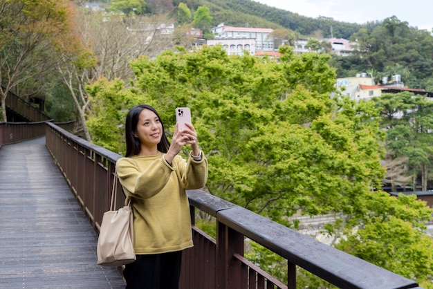 사진 관광객 여성이 휴대전화를 사용하여 숲의 산책로에서 사진을 찍습니다.