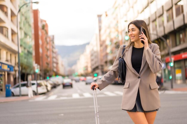 電話で概念の休暇のライフ スタイルを笑顔の街でスーツケースを持つ観光客の女性